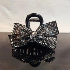 Detailed view of medium black hair claw clip with sparkling rhinestone bow on glossy surface