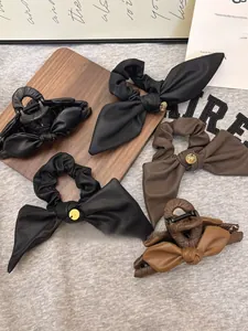 Dettaglio di fermagli e elastici per capelli in pelle con decori dorati su sfondo grigio