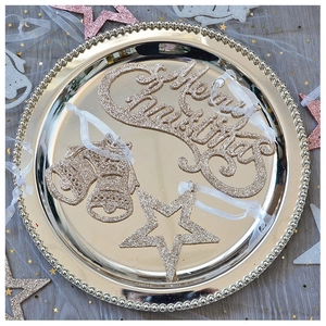 Macro detail of Merry Christmas gold and champagne glitter charms on a metallic tray