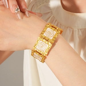 Close-up of a vintage golden square bracelet with white enamel spiral patterns on a model