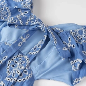 Detailed close-up of sky blue midi dress featuring white eyelet embroidery and tie-up neckline