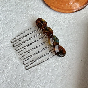 Tortoiseshell hair comb detail, resin twisted design with metal tines for chic hairstyles.