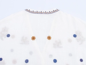 Detail of white V-neck shirt with blue and orange floral embroidery and scalloped edges