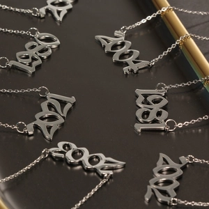 Detailed view of silver stainless steel year necklaces with gothic font on black tray