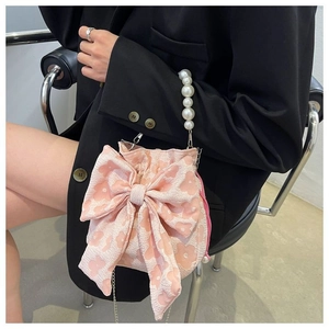 Pink bow bag with pearl handle and metal chain shown on model in black suit