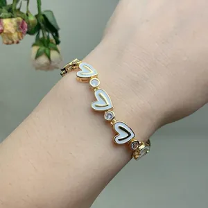 Detail of gold heart link bracelet with white enamel inlay and sparkling zircon stones