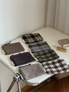 Close-up of assorted plaid fabric pouches with zipper and branded tags on a white table