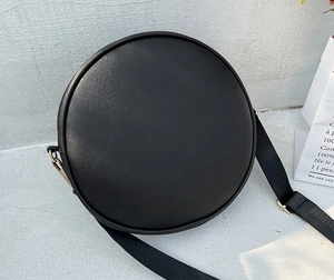 Detail of a black quilted round crossbody bag with matching wide shoulder strap and metal rings