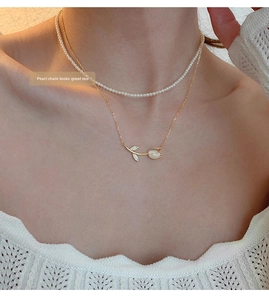 Close-up of white tulip pendant necklace paired with a layered pearl strand on model