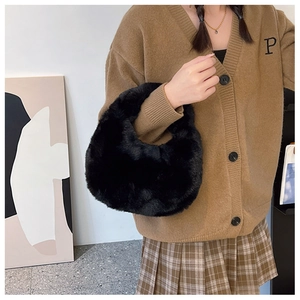 Close-up of fluffy black faux fur crescent hobo bag held by a model in a knit cardigan