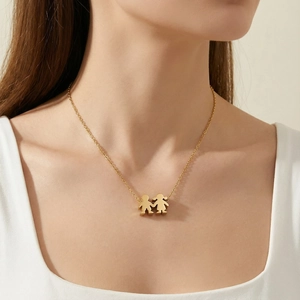 Detail of a gold stainless steel necklace with a cute boy and girl pendant worn by a model