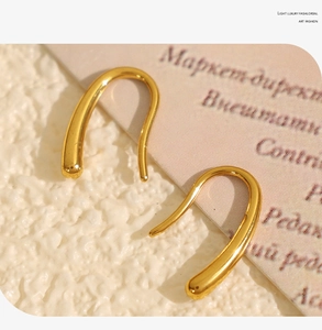 Vue macro de boucles d'oreilles crochet en U dorées sur un fond texturé minimaliste