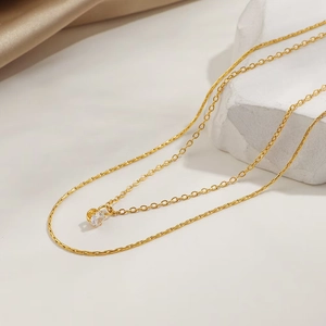 Double-layered gold titanium necklace with a sparkling round zircon on white silk background