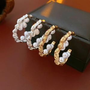 Macro view of C-shaped gold and silver earrings featuring pearls and twisted metal texture