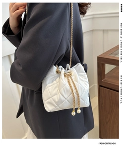 Close-up of white quilted bucket bag with gold chain and elegant pearl drawstring detail