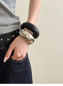 Close-up of minimalist matte black and polished silver wide chunky metal bangles