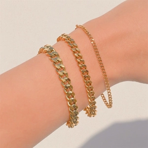 Close-up of three layered gold Cuban chain bracelets on model wrist in warm lighting