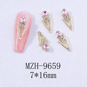 Macro detail of V-shaped gold alloy nail charms with pink teardrop crystal and tiny rhinestones