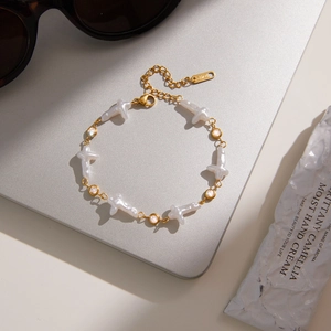 Detailaufnahme von goldenem Edelstahl-Perlenarmband mit Kreuz auf Silberlaptop