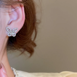 Close-up of sparkling hollow butterfly stud earrings in silver on woman's earlobe