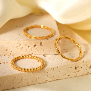 Three-piece set of golden stainless steel twist and beaded stackable rings on stone stand
