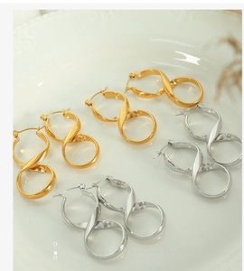 Detailed view of polished gold and silver infinity twist hoop earrings on a ceramic tray
