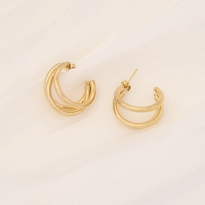 Detailed view of gold triple hoop earrings with polished metal finish on white silk