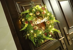 Detail of Christmas wreath with warm LED lights and wooden Welcome sign on front door