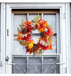 Autumn wreath with red sunflowers, maple leaves, and pumpkins on a white front door