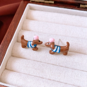 Makroaufnahme von Cartoon-Dackeln-Ohrringen mit brauner Emaille und blauem Streifen