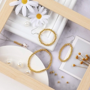 Flat lay of gold beaded bracelet and hoop earrings set on white marble with flowers