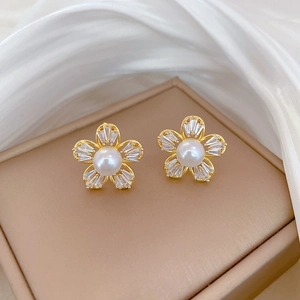 Close-up of gold flower earrings with white pearl center and zircon crystal petals