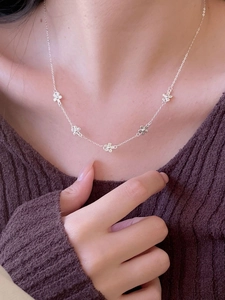 Close-up of minimalist 925 silver necklace with five small floral charms on model's collarbone