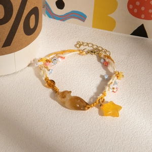 Handmade woven bracelet with orange resin cat and star pendants on a textured surface
