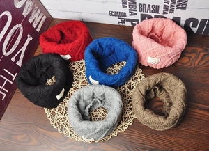 Flat lay of knit kids' neck warmers in six colors with diamond pattern on a wooden table