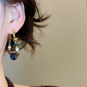 Detail of beaded hoop earring with tiger eye and blue stone on model ear