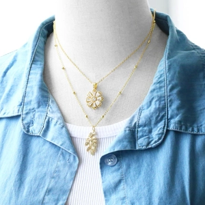 Layered gold necklace featuring daisy and leaf pendants worn on a stylish casual outfit