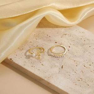Close-up of gold plated rings featuring Love lettering, pearls and zircon on silk fabric
