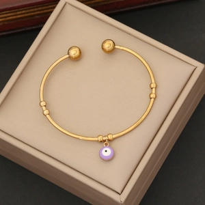 Detail of gold open bangle featuring a purple enamel evil eye charm in a gift box