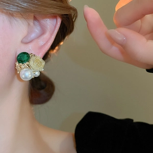 Vue détaillée de boucles d'oreilles camélia dorées avec cristal émeraude et perles sur mannequin