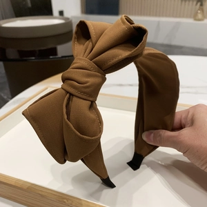 Detail of a brown fabric headband featuring a large bow and non-slip black end tips
