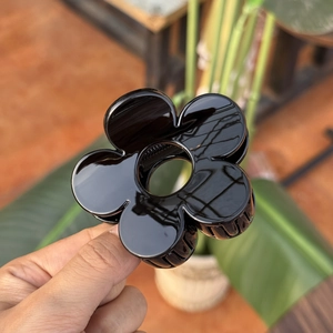 Détail d'une pince à cheveux fleur noire brillante tenue sur un fond de verdure naturelle