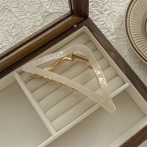 Detail van een witte haarklem met schelppatroon in een houten sieradendoosje op textiel