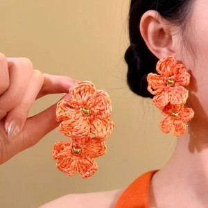 Close-up of hand-woven orange flower earrings showing intricate craft detail