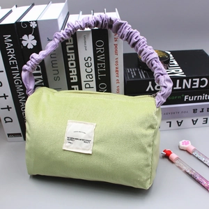 Detail of light green corduroy handbag with purple scrunchie handle on books