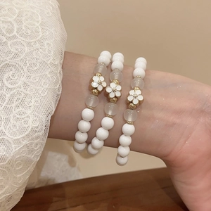 Three-piece acrylic beaded flower bracelet set with white enamel daisy charms worn on wrist