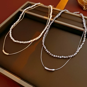 Close-up of double-layered gold and silver necklaces with pearls and curved tube pendants