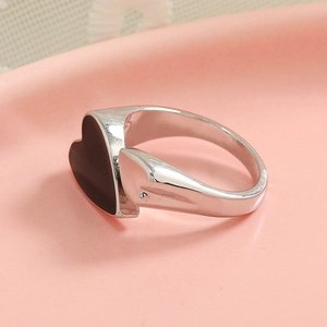 Minimalist silver open ring with black enamel heart charm on a decorative tray