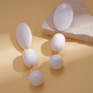 Détail de boucles d'oreilles blanches en acrylique avec anneaux dorés sur fond de pierre