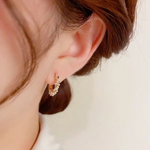 Macro shot of C-shaped golden hoop earrings with wrapped baroque pearls on model